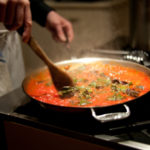 Motion blur photograph of chef stirring pasta sauce on stove.